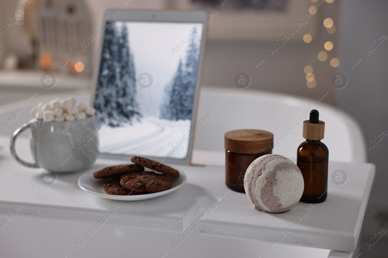 Photo of White wooden tray with tablet, cookies and spa products on bathtub in bathroom