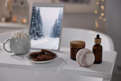 White wooden tray with tablet, cookies and spa products on bathtub in bathroom