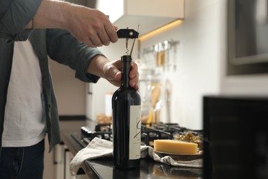 Photo of Man opening wine bottle with corkscrew at black countertop indoors, closeup