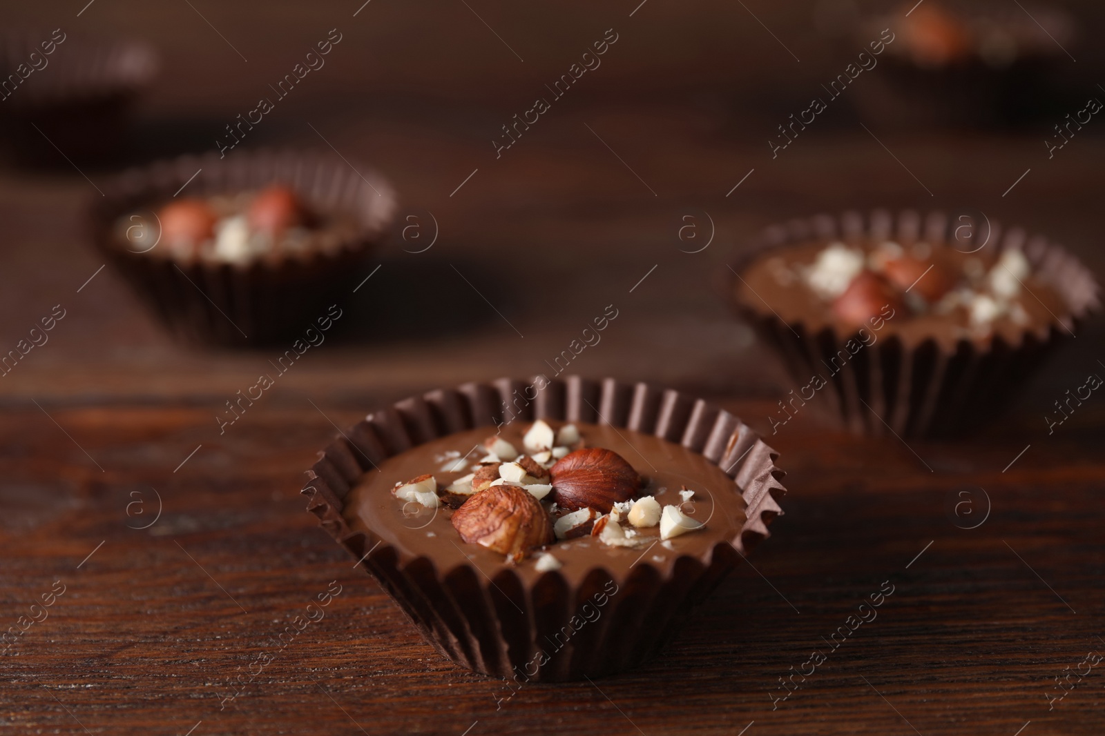 Photo of Delicious chocolate candies with hazelnuts on wooden table, closeup