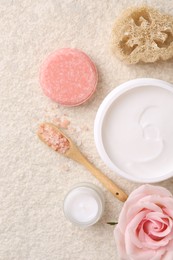 Flat lay composition with moisturizing cream in open jar and other body care products on light textured table