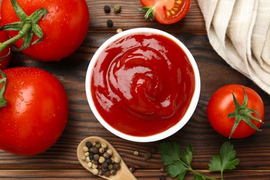 Photo of Delicious ketchup in bowl, tomatoes and peppercorns on wooden table, flat lay