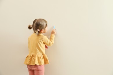 Little girl drawing on beige wall, back view and space for text. Child`s art