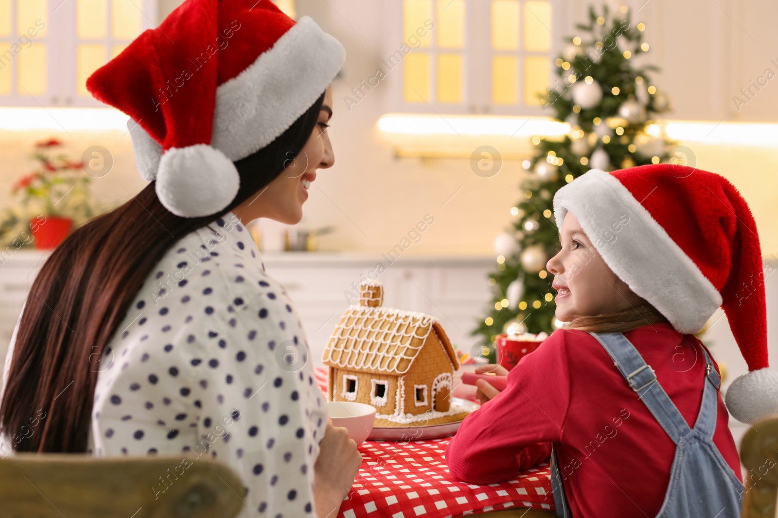 Photo of Mother and daughter decorating gingerbread house at table indoors