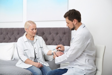 Doctor checking mature woman's pulse with medical device in bedroom