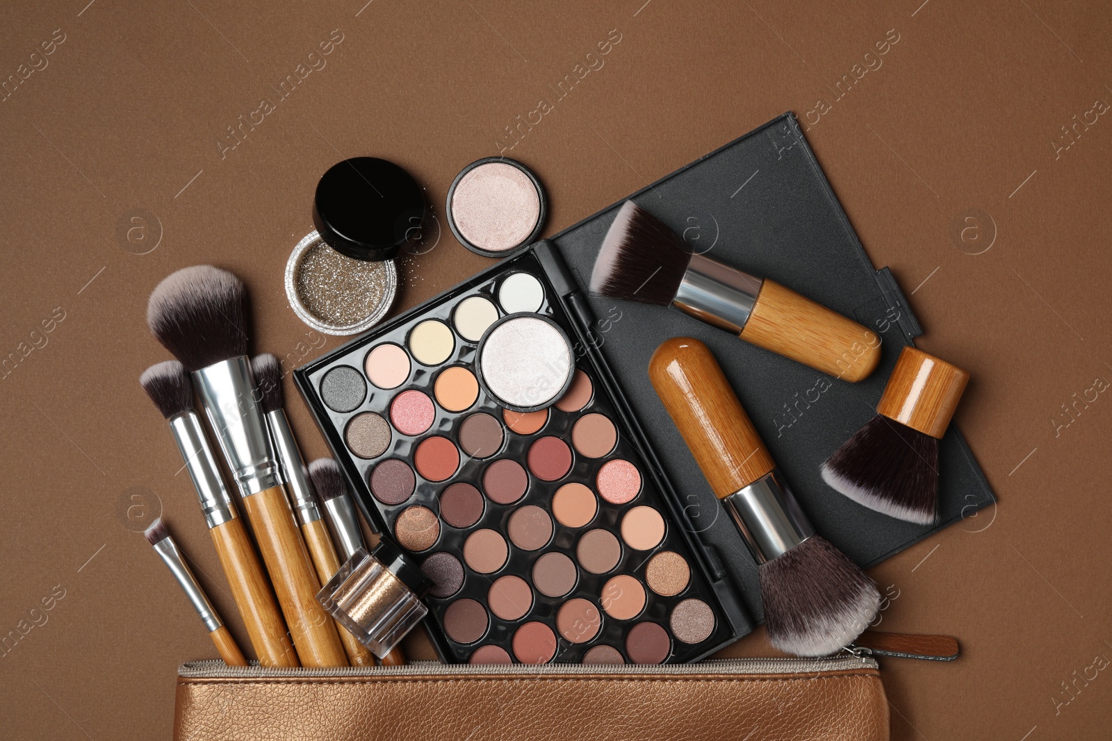 Photo of Cosmetic bag with makeup products and beauty accessories on brown background, flat lay