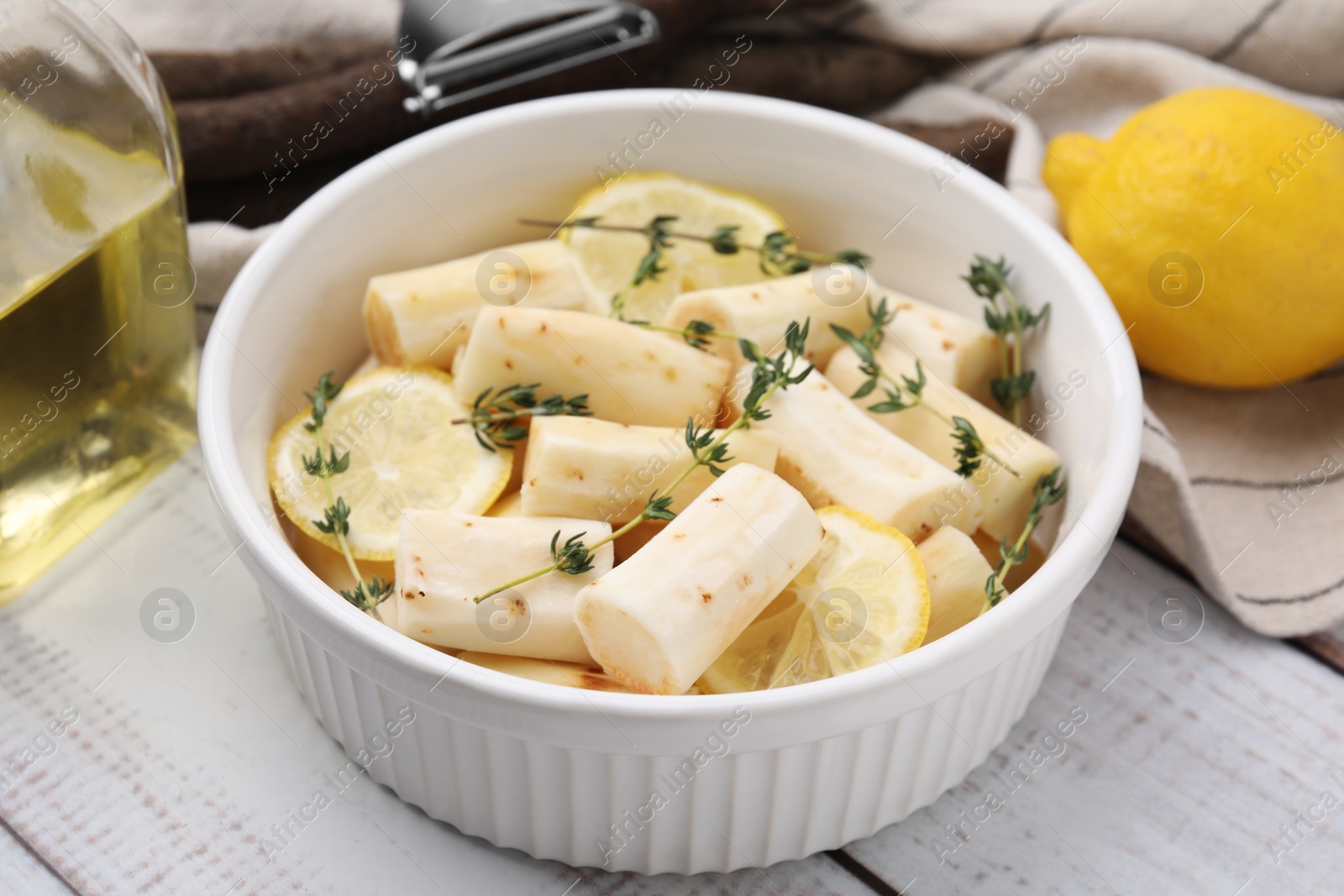 Photo of Dish with raw salsify roots, lemon and thyme on white wooden table, closeup