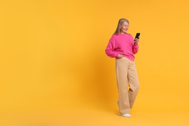 Senior woman with phone on orange background, space for text