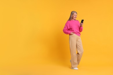 Photo of Senior woman with phone on orange background, space for text