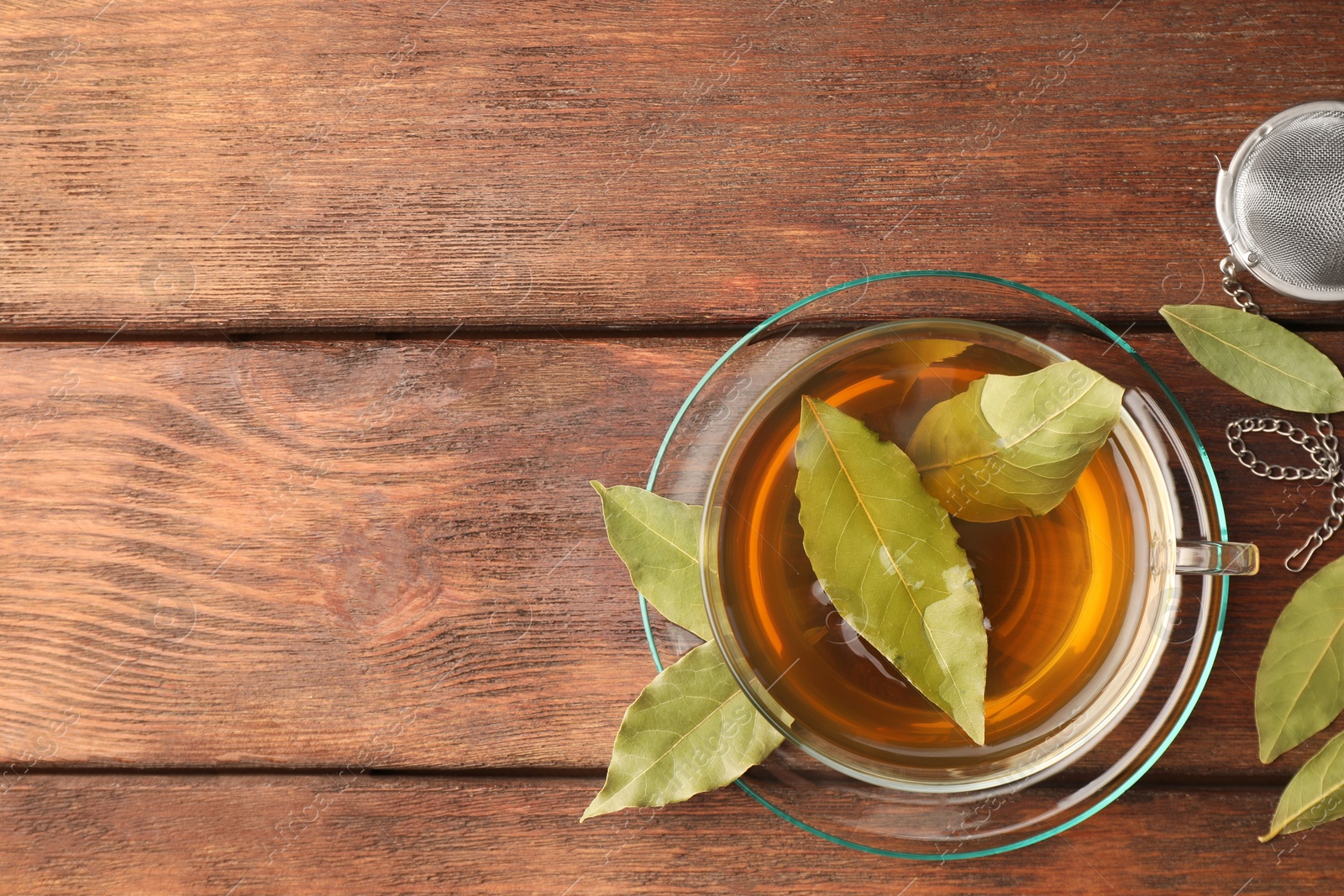 Photo of Cup of freshly brewed tea with bay leaves on wooden table, flat lay. Space for text