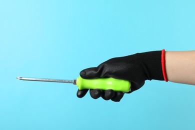 Woman holding screwdriver on light blue background, closeup