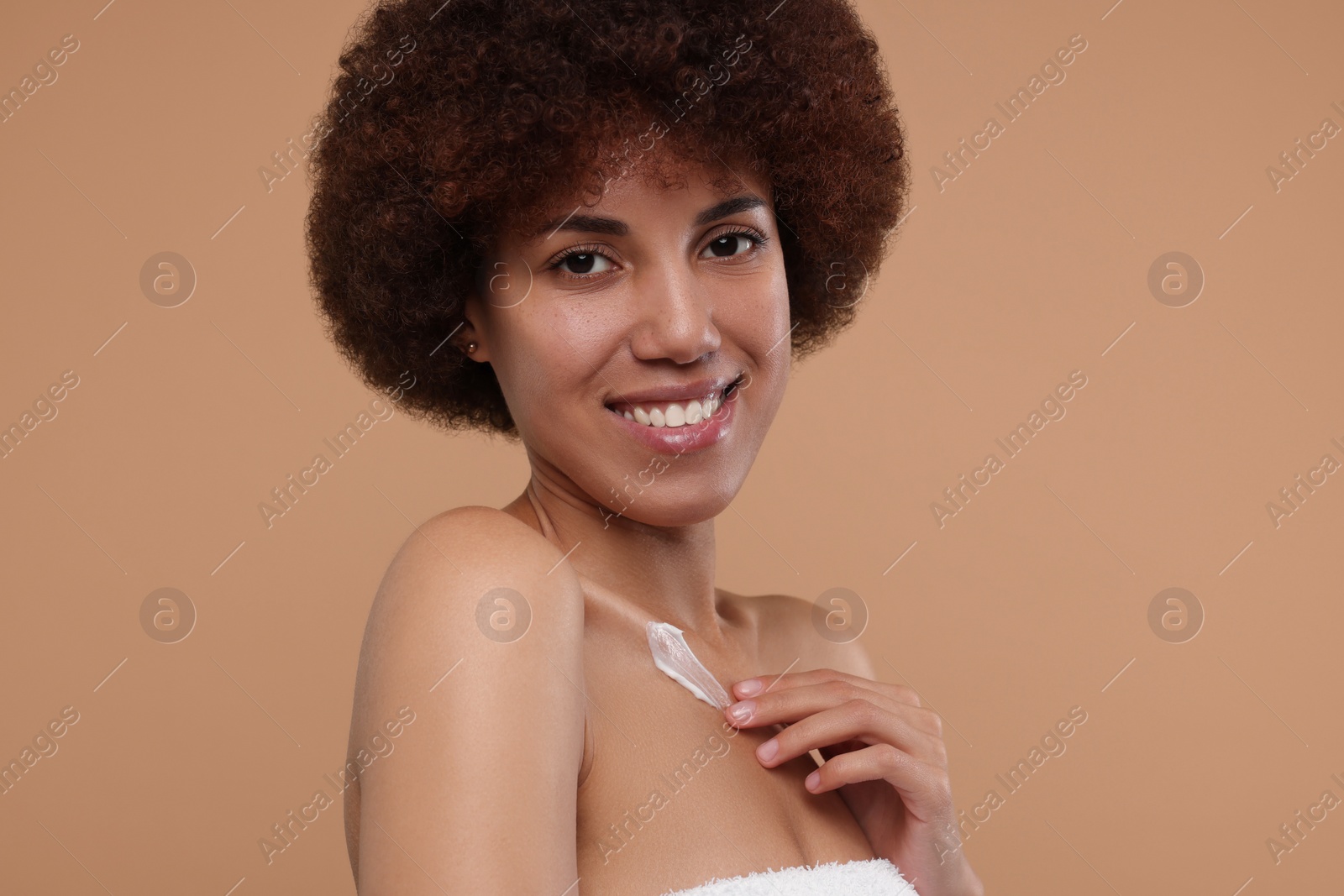 Photo of Beautiful young woman applying cream onto body on beige background