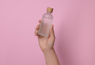 Photo of Woman holding bottle of cosmetic product on pink background, closeup