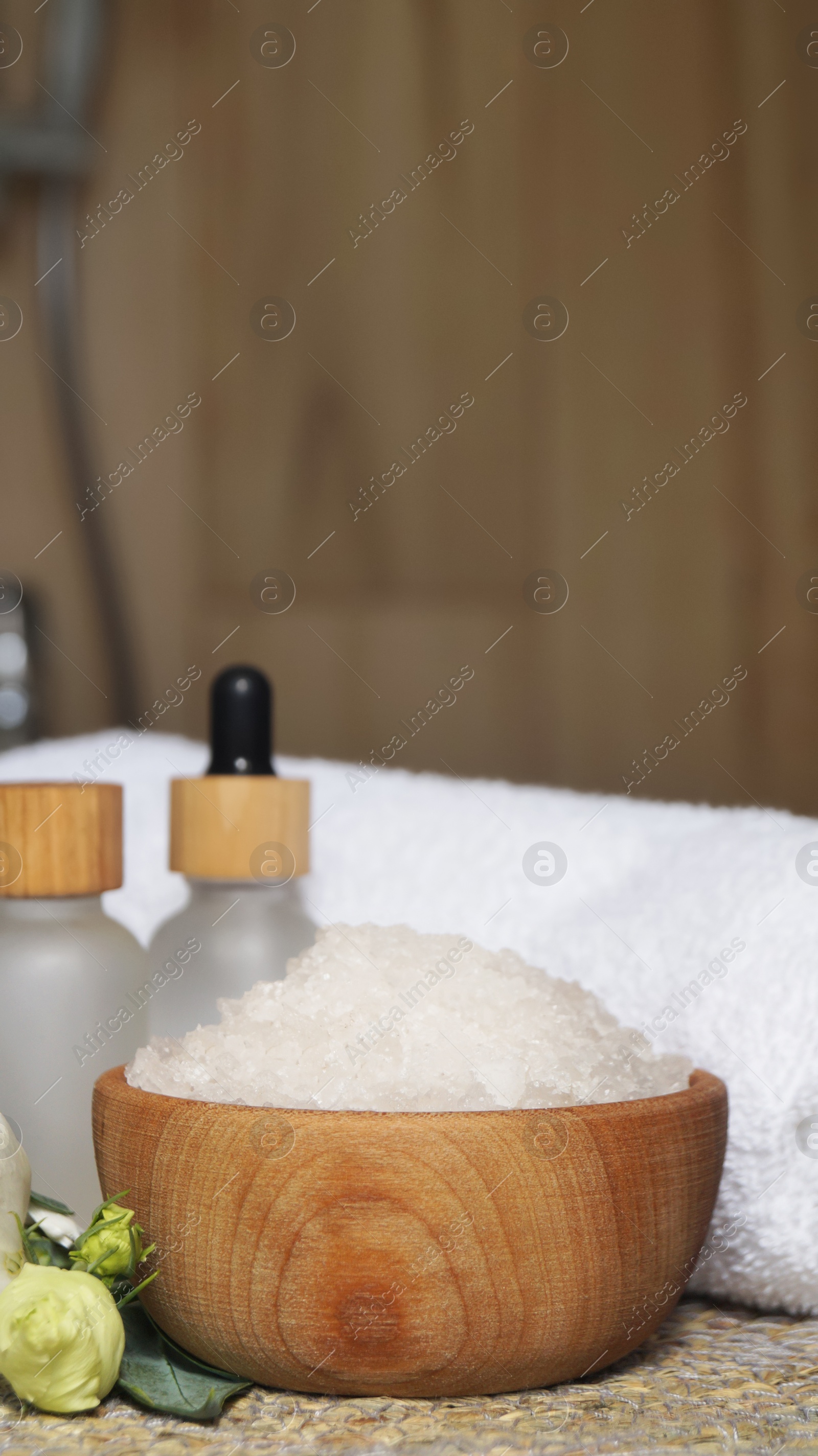 Photo of Bowl with bath salt and cosmetic product near fluffy towel on wicker mat indoors