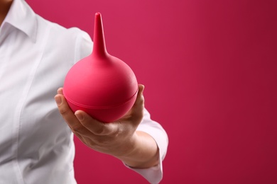 Photo of Woman holding enema on pink background, closeup. Space for text