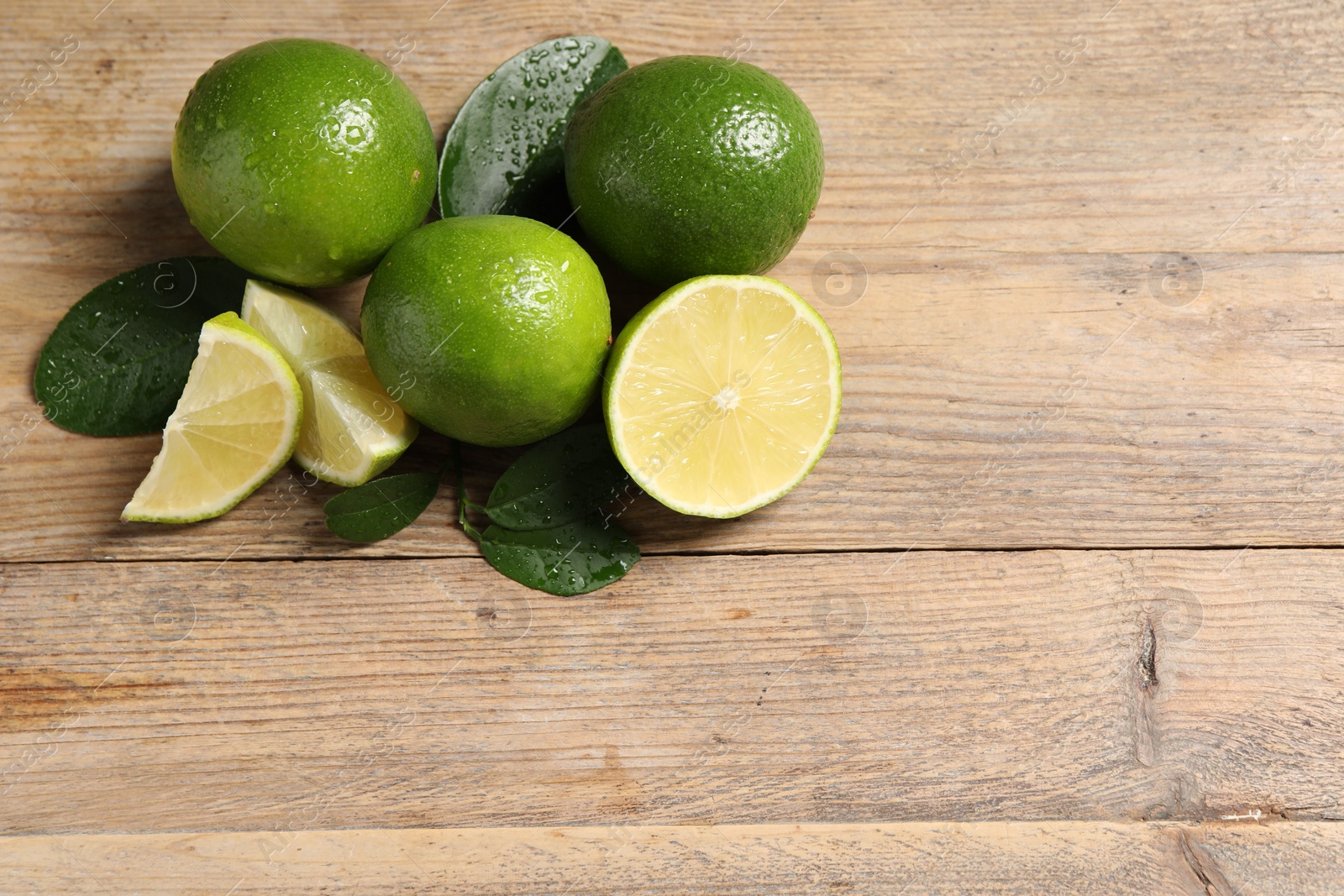 Photo of Fresh ripe limes and green leaves with water drops on wooden table, flat lay. Space for text