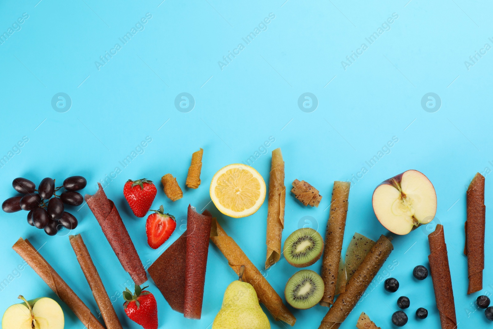 Photo of Flat lay composition with delicious fruit leather rolls on light blue background. Space for text