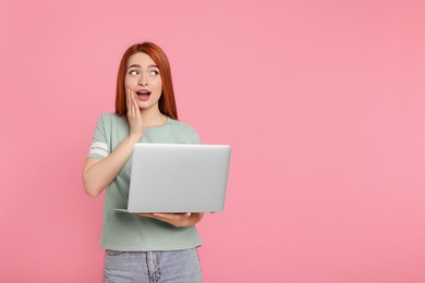 Photo of Surprised young woman with laptop on pink background, space for text