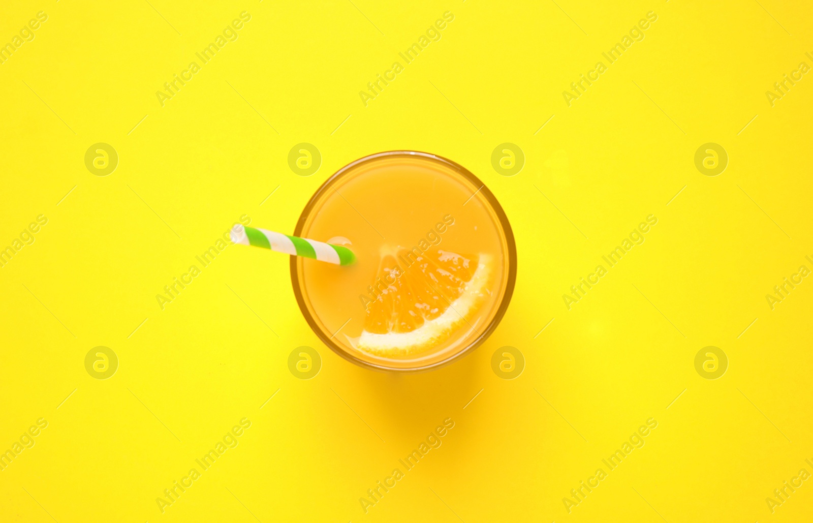 Photo of Glass of orange juice on yellow background, top view