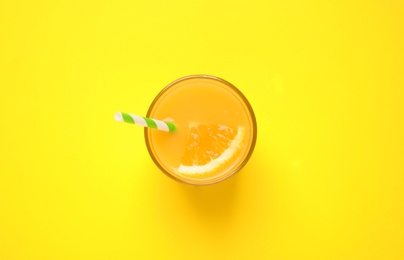 Photo of Glass of orange juice on yellow background, top view