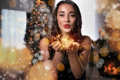 Image of Beautiful young woman wearing elegant dress blowing kiss in room decorated for Christmas