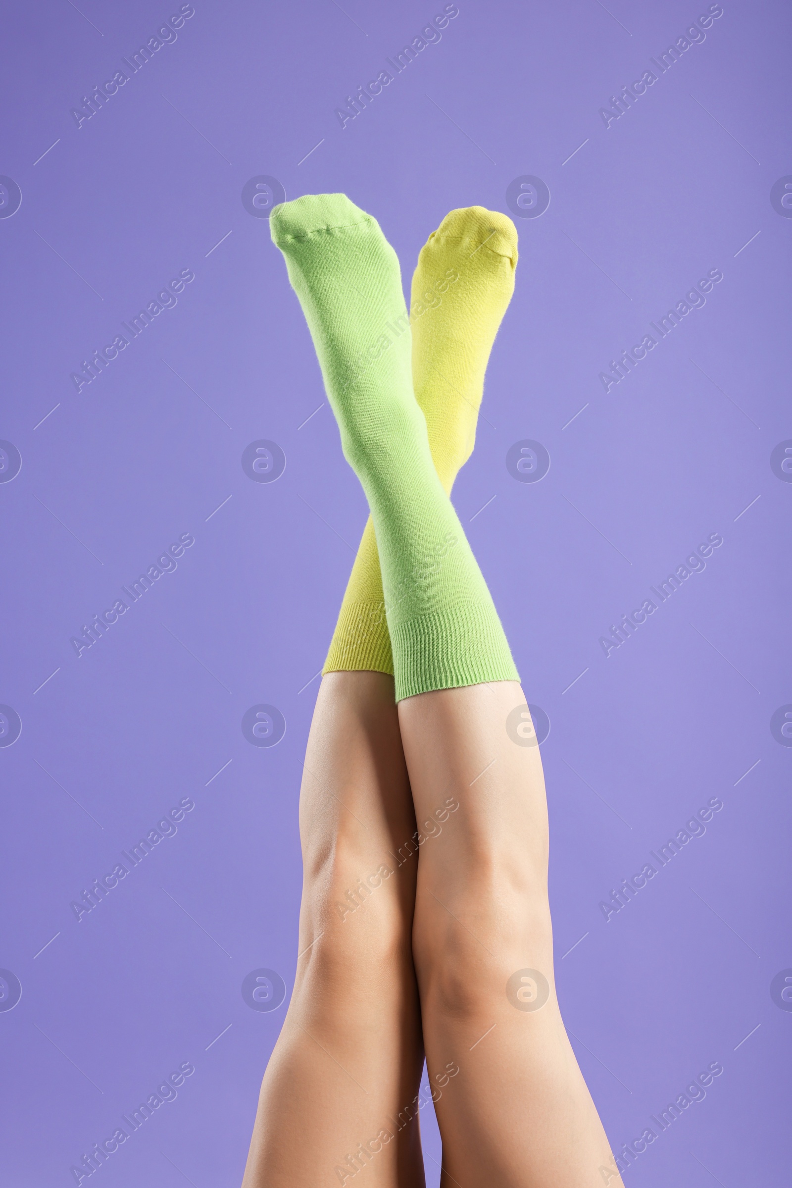 Photo of Woman in different stylish socks on violet background, closeup