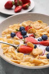 Photo of Bowl of tasty crispy corn flakes with milk and berries on light grey table, closeup