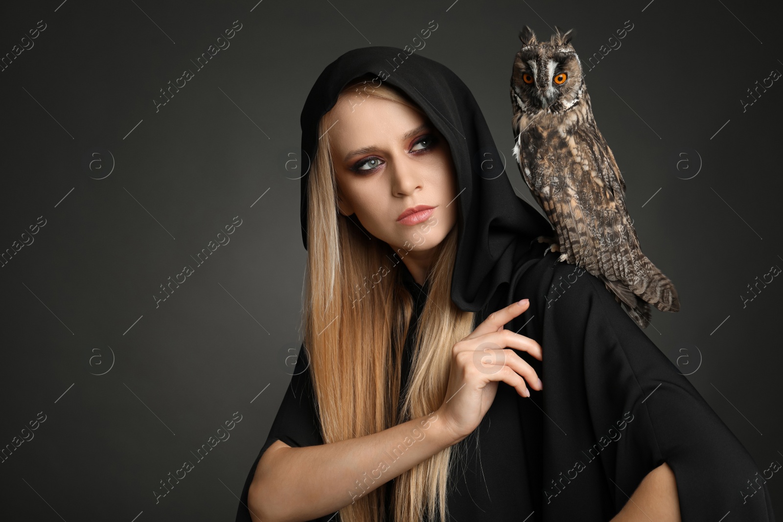 Photo of Witch in black mantle with owl on dark background. Scary fantasy character