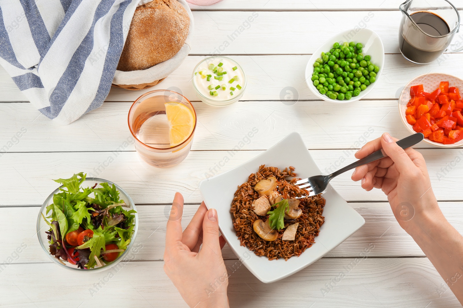 Photo of Woman eating tasty brown rice with meat and vegetables at white wooden table, closeup