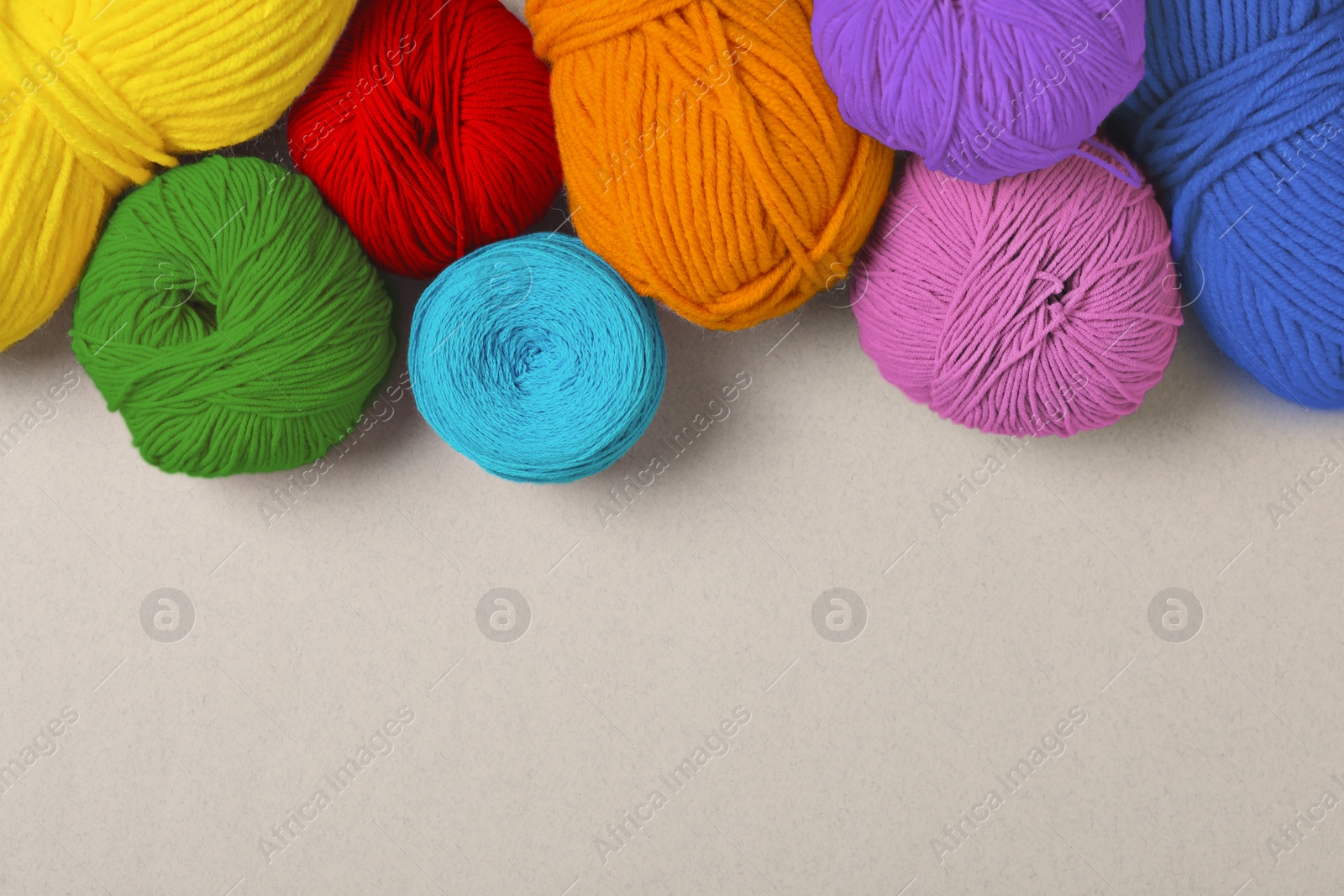 Image of Balls of yarn in rainbow colors on light background, flat lay. Space for text