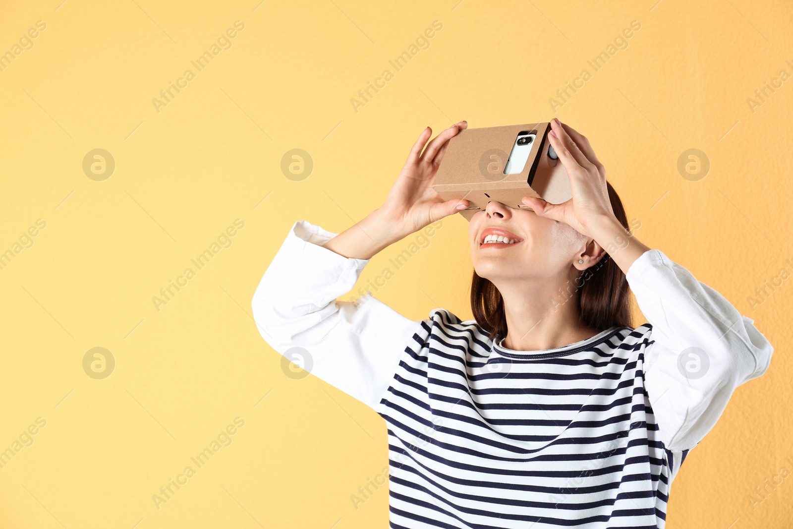 Photo of Young woman using cardboard virtual reality headset on color background. Space for text