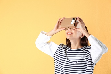 Young woman using cardboard virtual reality headset on color background. Space for text