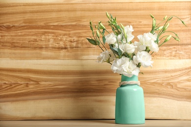 Photo of Vase with beautiful flowers on table against wooden background, space for text