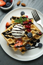 Photo of Delicious Belgian waffles with ice cream, berries and chocolate sauce served on grey textured table, flat lay