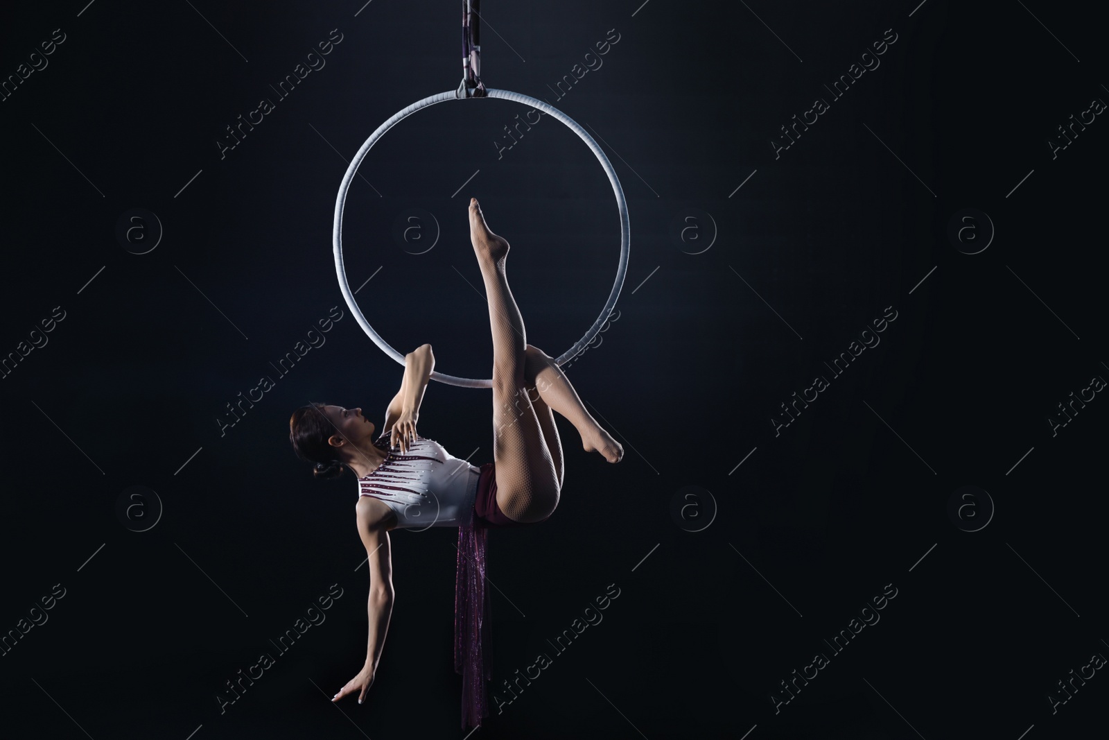 Photo of Young woman performing acrobatic element on aerial ring indoors