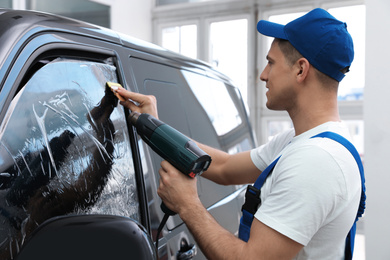 Worker tinting car window with foil in workshop