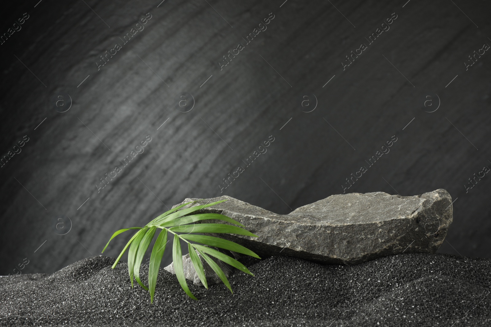 Photo of Presentation of product. Stone podium and palm leaves on black sand against dark textured background. Space for text