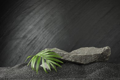 Presentation of product. Stone podium and palm leaves on black sand against dark textured background. Space for text