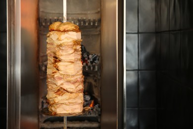 Photo of Vertical rotisserie with roasted meat in restaurant kitchen. Space for text