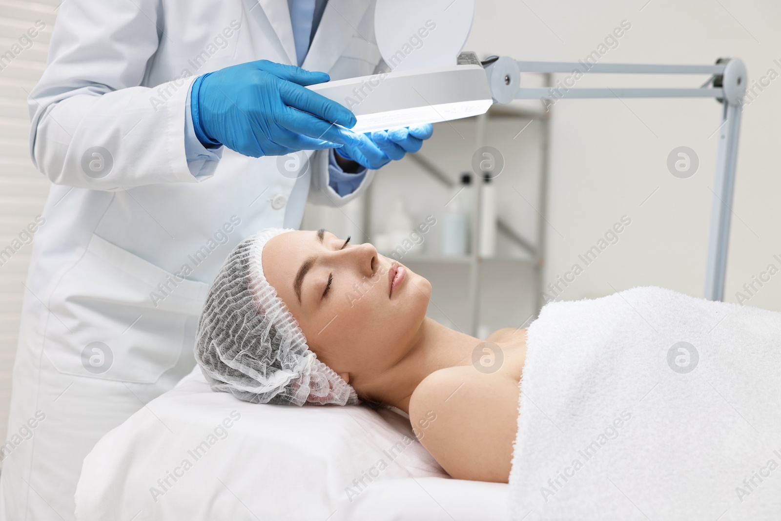 Photo of Dermatologist examining patient`s face under lamp in clinic, closeup