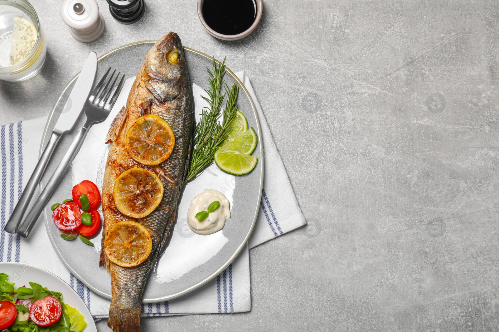 Photo of Delicious baked sea bass fish served with lemon, rosemary and sauce on light grey table, flat lay. Space for text