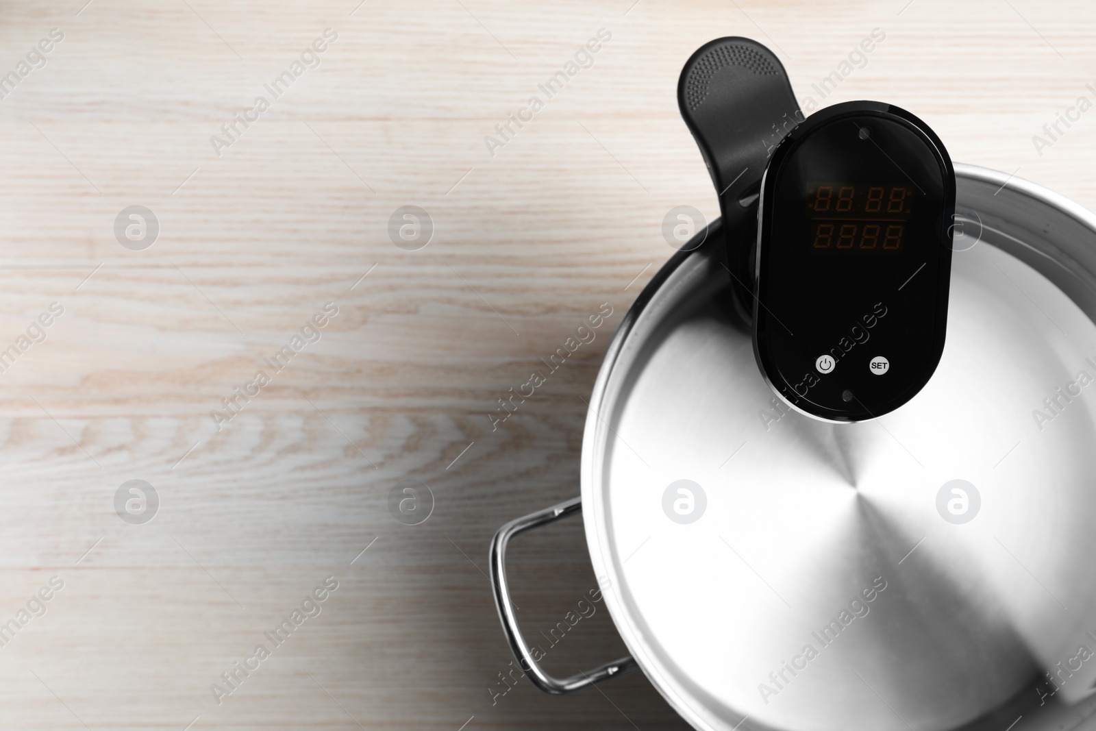 Photo of Thermal immersion circulator in pot on white wooden table, top view with space for text. Sous vide cooker