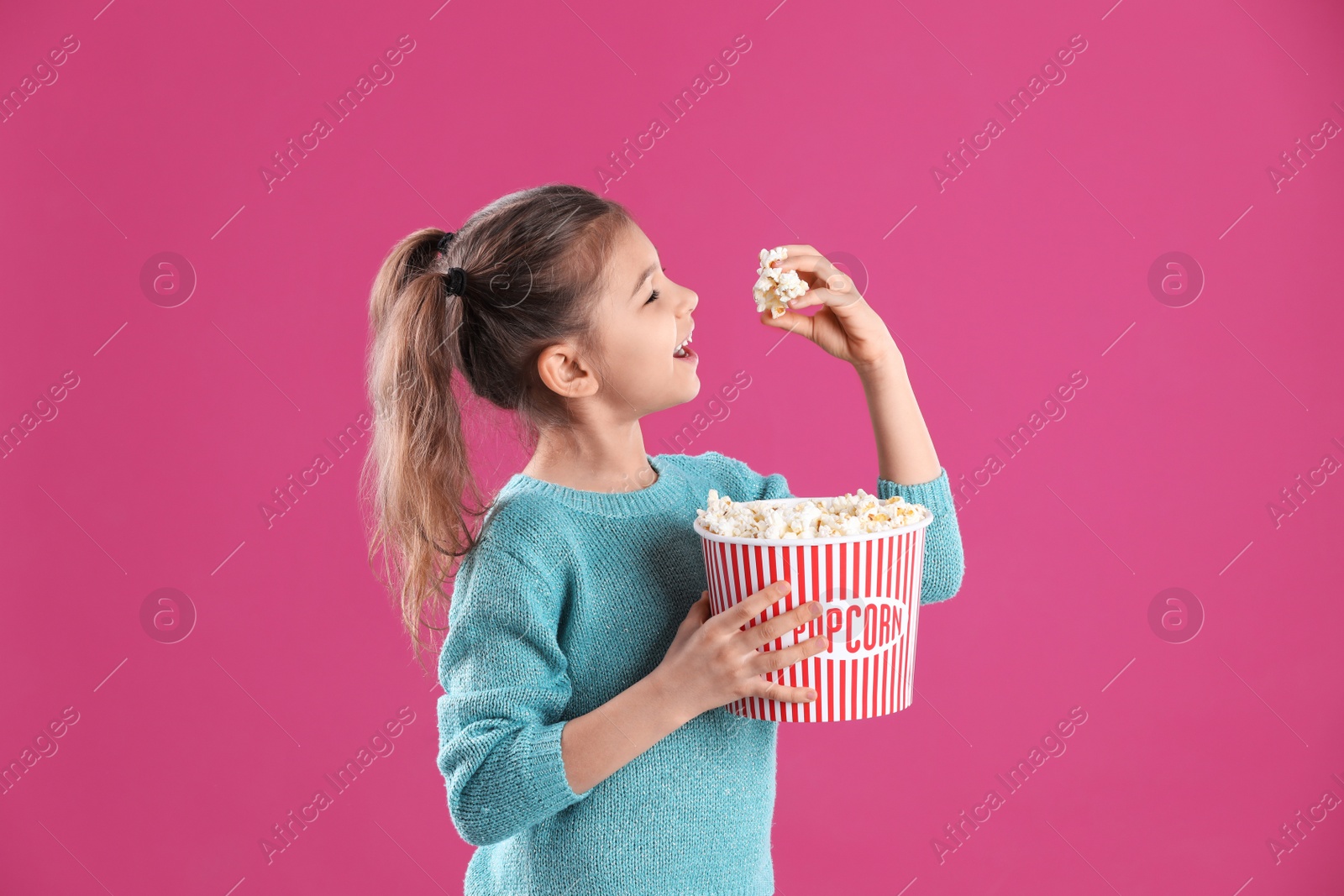 Photo of Cute little girl with popcorn on color background
