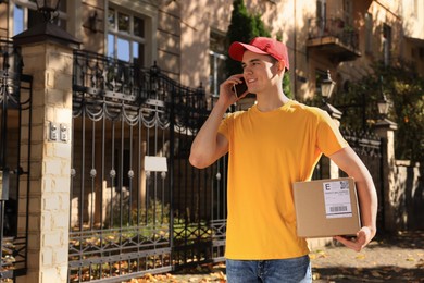 Photo of Courier with parcel talking by smartphone on city street