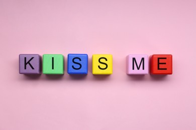 Photo of Colorful cubes with phrase Kiss Me on pink background, flat lay