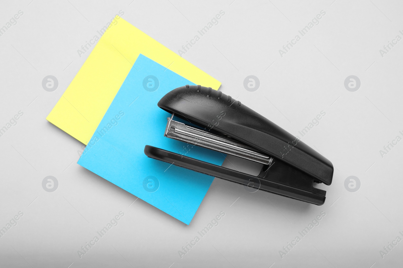 Photo of New bright stapler with sticky notes on light grey background, flay lay