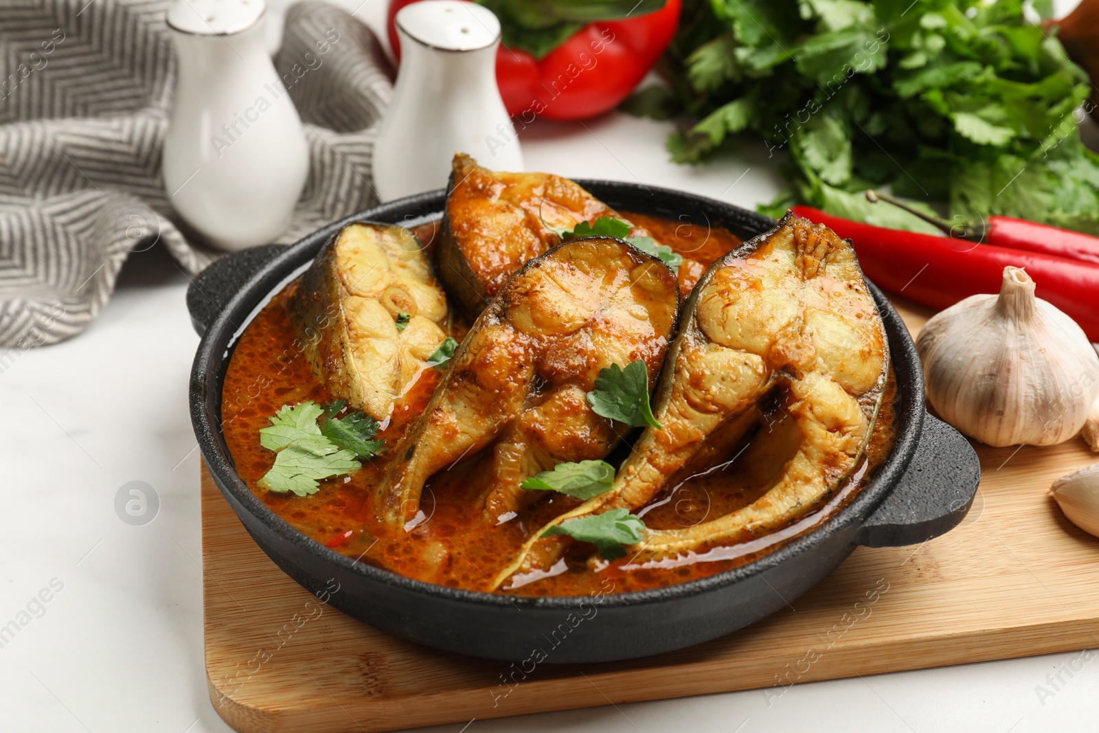 Photo of Tasty fish curry and ingredients on white table, closeup. Indian cuisine