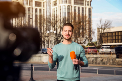 Image of Young male journalist with microphone working on city street