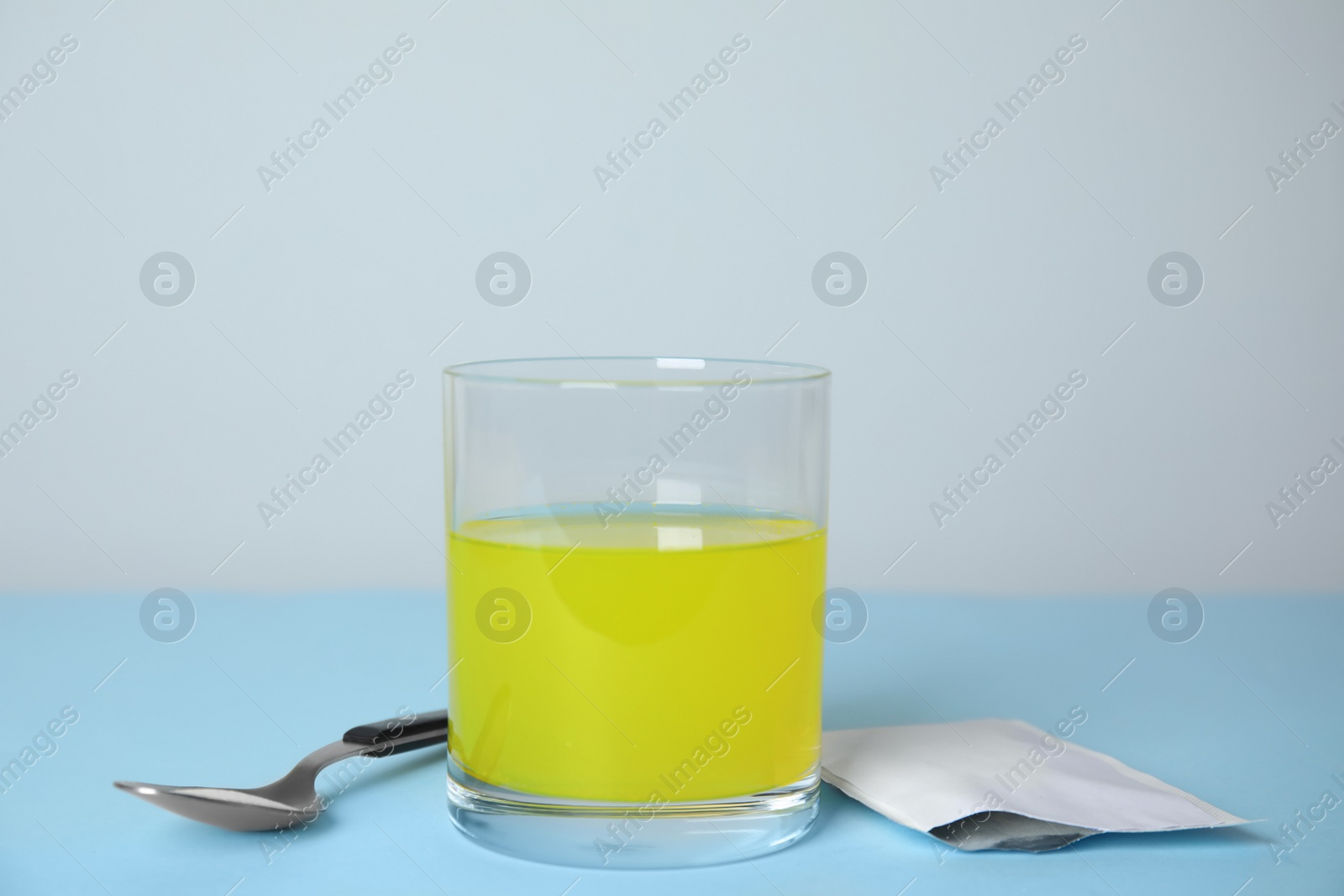 Photo of Glass of dissolved medicine, sachet and spoon on turquoise table