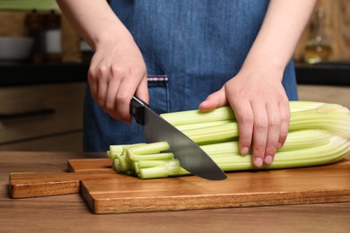 Photo of Woman cutting fresh green celery at wooden table, closeup
